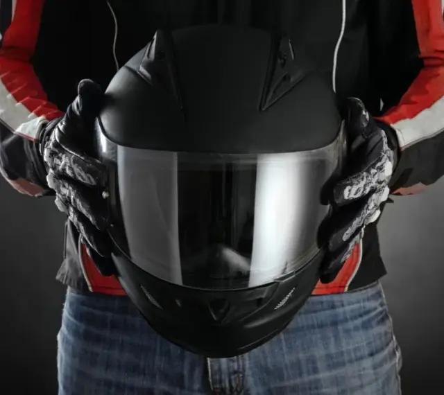 Persona con guantes de moto sostiene casco negro. Se aprecian detalles de las medidas exteriores casco moto en su diseño.