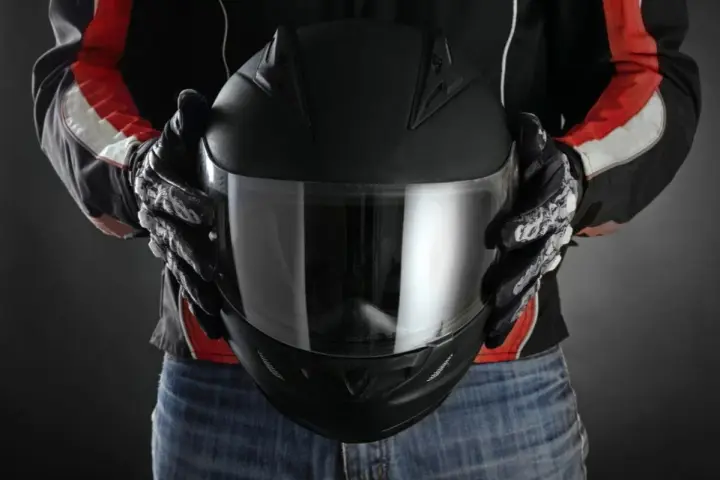 Persona con guantes de moto sostiene casco negro. Se aprecian detalles de las medidas exteriores casco moto en su diseño.