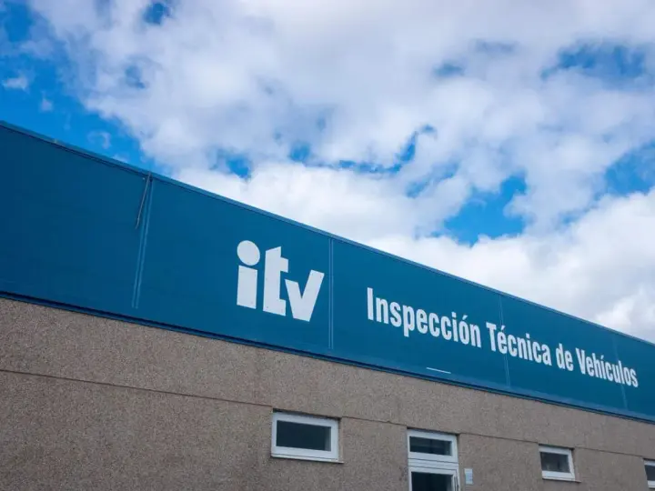 Edificio de la ITV bajo un cielo azul con nubes. El letrero blanco dice "itv Inspección Técnica de Vehículos".