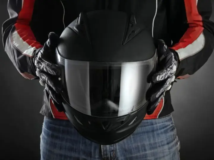 Persona con guantes de moto sostiene casco negro. Se aprecian detalles de las medidas exteriores casco moto en su diseño.