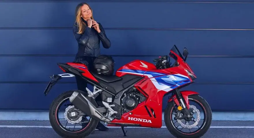 Mujer con chaqueta de cuero junto a una moto deportiva roja Honda. Ideal para quienes buscan motos tetracilindricas a2.