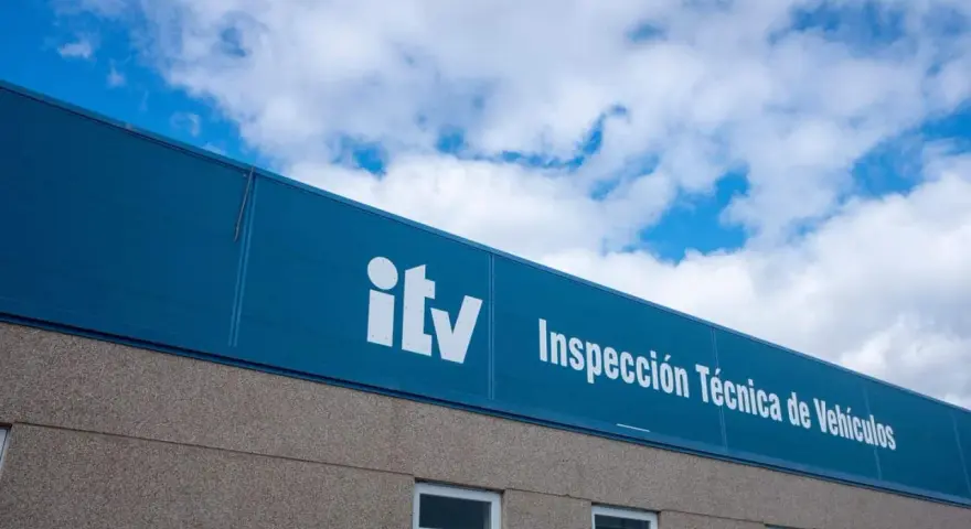 Edificio de la ITV bajo un cielo azul con nubes. El letrero blanco dice "itv Inspección Técnica de Vehículos".