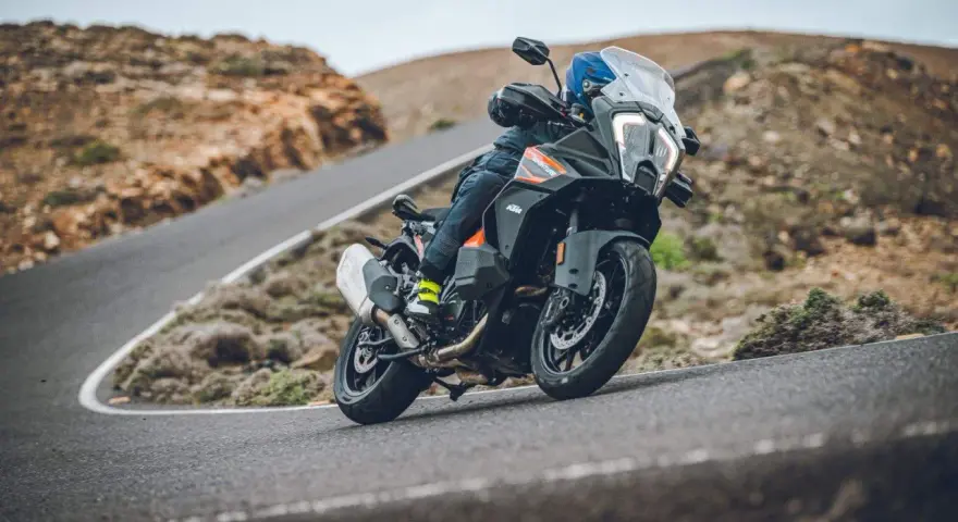 Motociclista en una KTM 1290 Adventure, inclinada en una curva de carretera montañosa. El peso de la moto se siente en la maniobra.