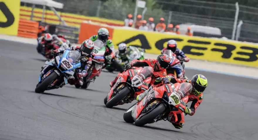 Motociclistas compiten en una carrera, con el número 65 en primer plano. El sbk calendario se acerca.