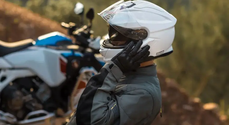 Motociclista ajustándose su casco modular silencioso blanco, listo para la aventura.