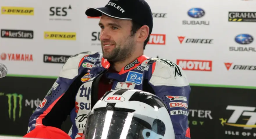 William Dunlop, piloto de motociclismo, sonríe con su casco de carreras y mono de competición.