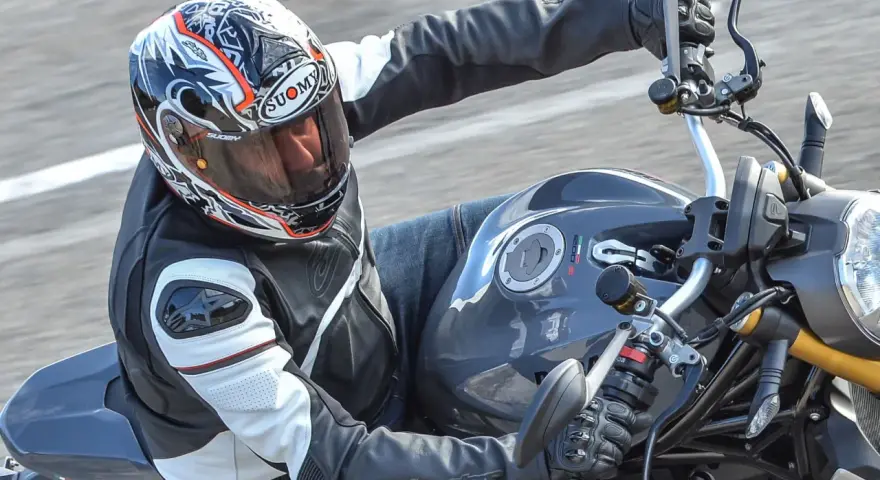Motociclista con casco Suomy, con diseño llamativo, en una moto deportiva. Las opiniones sobre cascos Suomy son positivas.