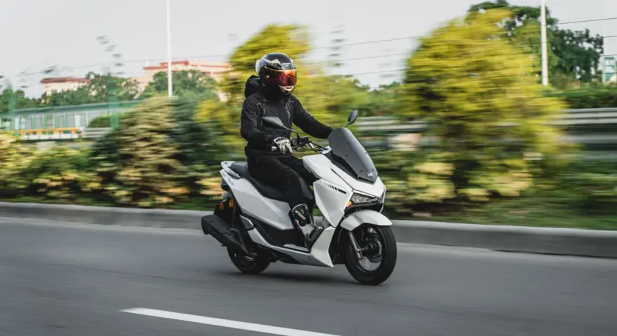 Persona conduce moto blanca con carnet B, disfrutando del paisaje borroso.