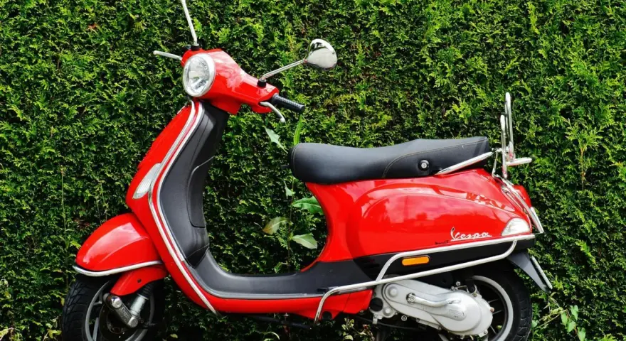 Scooter roja aparcada frente a un seto verde. Ideal para entender las diferencias carnet a1 y a2.