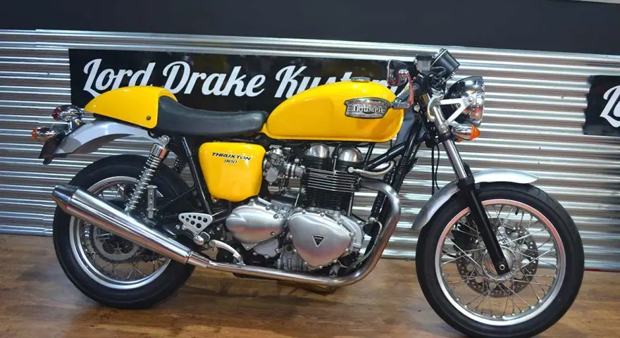 Motocicleta Triumph Thruxton 900 amarilla, estilo café racer, lista para la carretera.