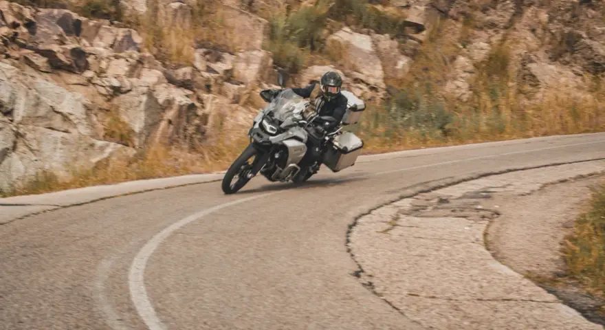 Motociclista en pruebas de motos, inclinado en una curva de carretera montañosa.