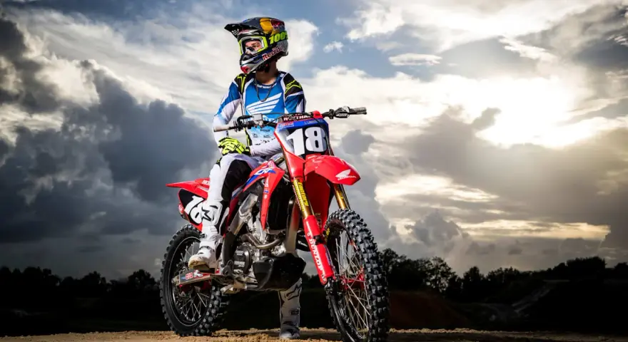 Jett Lawrence, piloto de motocross, posa con su moto roja bajo un cielo dramático.