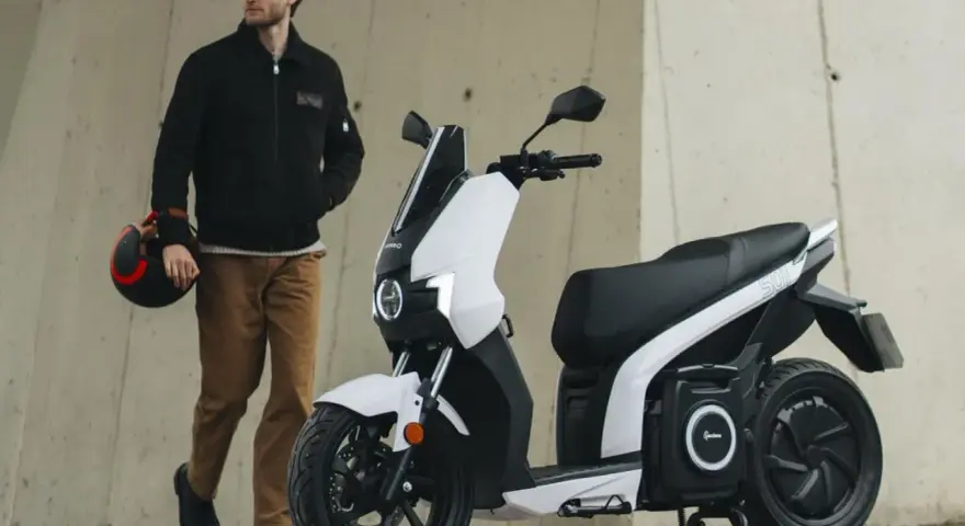 Hombre con casco junto a un scooter eléctrico blanco, el scooter mas potente para la ciudad.