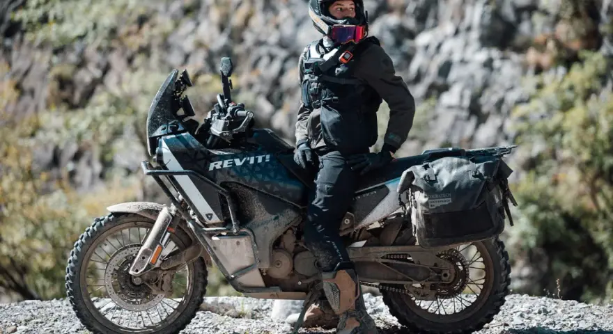 Motociclista con chaqueta REV'IT! y equipo de aventura, listo para aprender como lavar chaqueta de moto después de un viaje polvoriento.