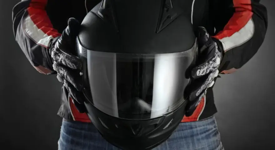 Persona con guantes de moto sostiene casco negro. Se aprecian detalles de las medidas exteriores casco moto en su diseño.