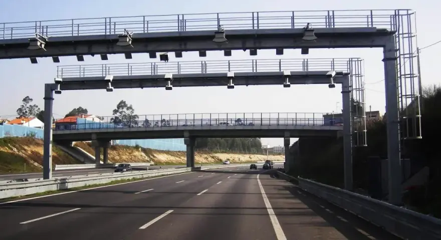 Un pórtico de peaje automático en España. Los coches circulan por la autopista bajo una estructura metálica con antenas.