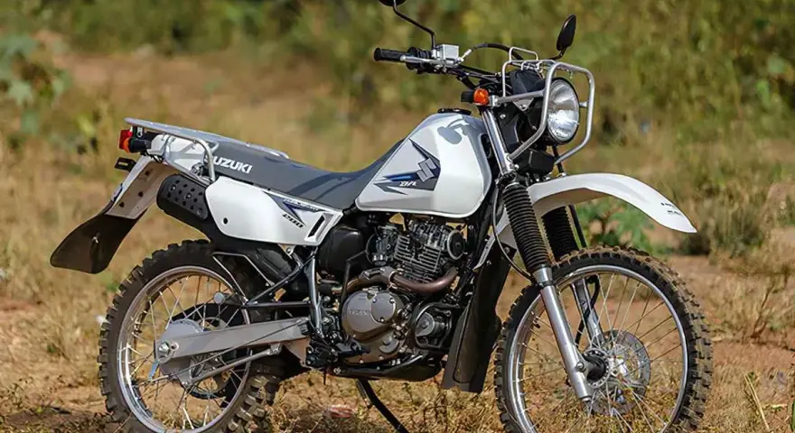 Suzuki DR 200 lista para la aventura. Moto blanca de doble propósito con neumáticos todoterreno, lista para explorar caminos rurales.