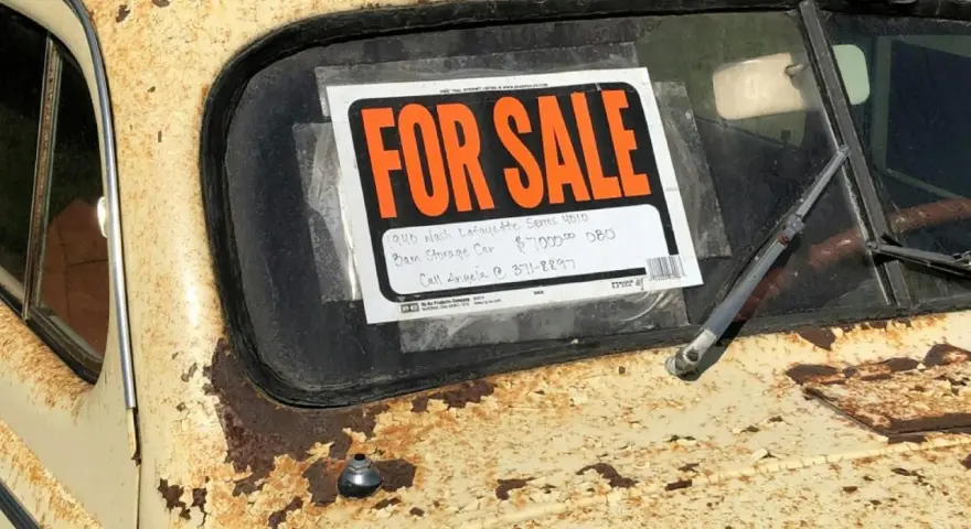 Coche antiguo a la venta, con cartel "FOR SALE". Para saber si una moto tiene cargas, revisa su historial.