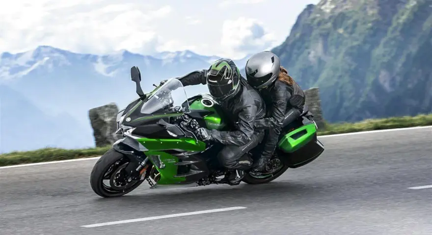 Pareja en una moto deportiva verde y negra, disfrutando de un viaje por carretera entre montañas. ¡Las mejores motos deportivas para aventuras!