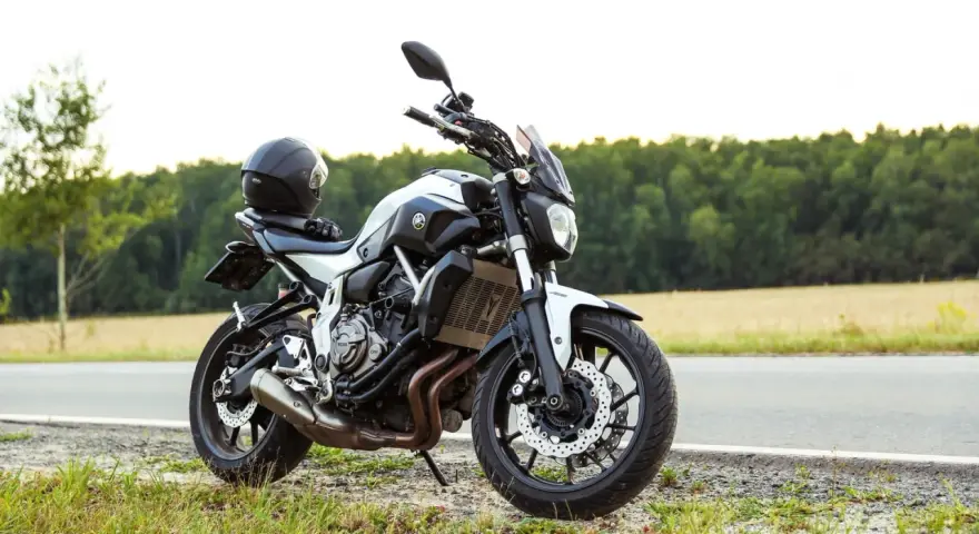 Una moto a2 blanca y negra, con un casco negro en el asiento, aparcada en la cuneta de una carretera rural.