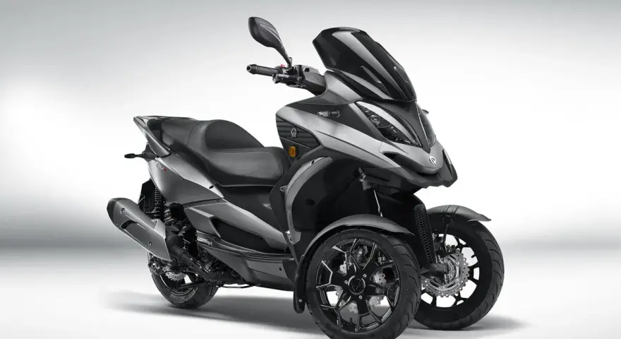 Triciclo gris moderno, estilo deportivo, con tres ruedas. El **Quadro QV3** es un vehículo ágil y seguro, ideal para sortear el tráfico urbano sin **problemas**.
