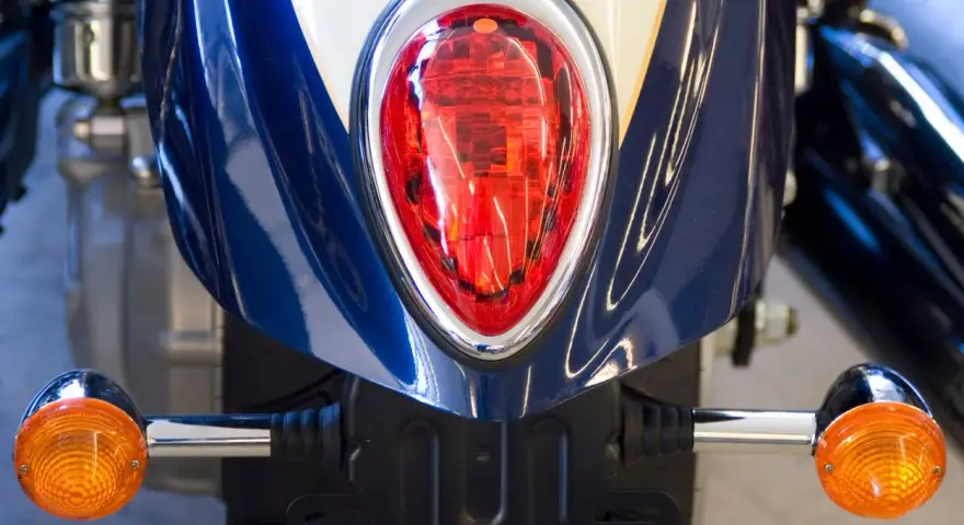 Detalle de la parte trasera de una moto azul y blanca, con intermitentes naranjas y luz roja. Podría ser una multa por llevar luces led moto.
