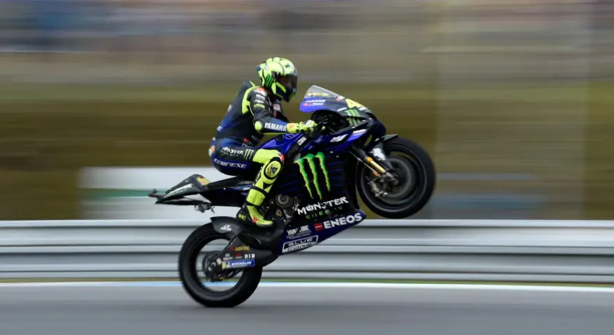 Valentino Rossi levanta la rueda trasera de su Yamaha en plena carrera, con su icónico casco amarillo y traje azul.