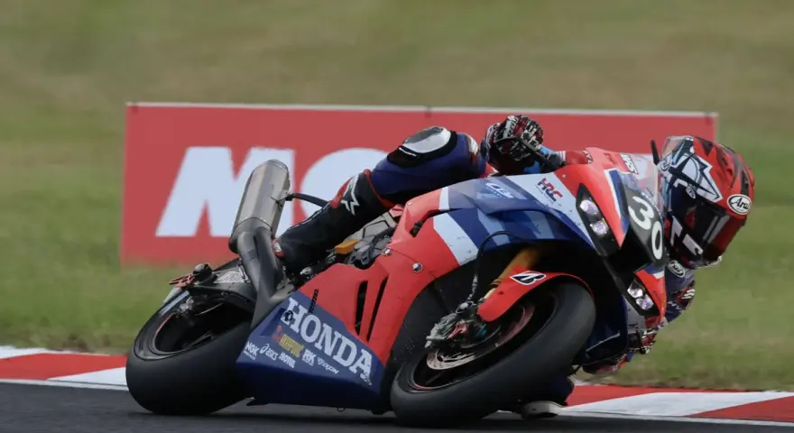 Piloto en moto Honda roja y azul inclinado en curva durante las 8 horas de Suzuka.