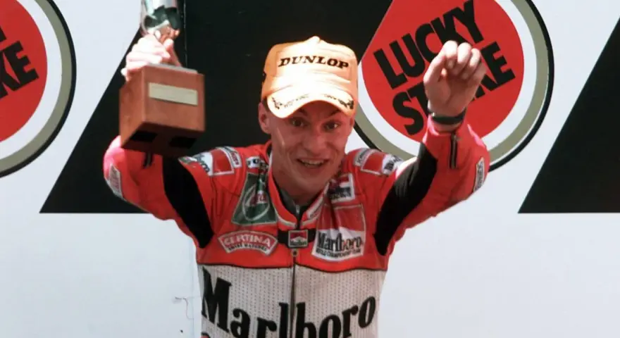 Ralf Waldmann, piloto de motos, celebra con un trofeo y un puño en alto, luciendo su traje de competición Marlboro.