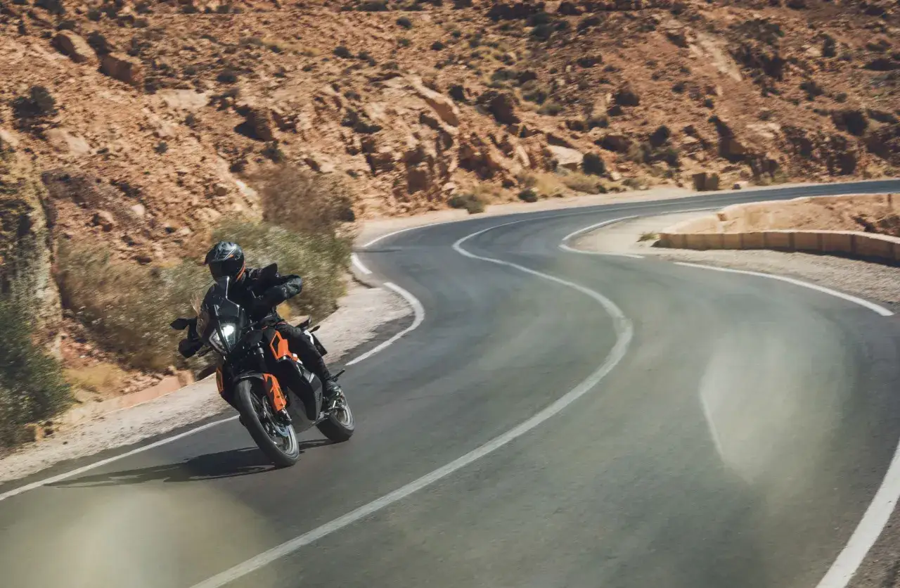 Motociclista en KTM 790 Adventure recorre una carretera sinuosa en un paisaje desértico. Las opiniones sobre esta moto son excelentes para la aventura.