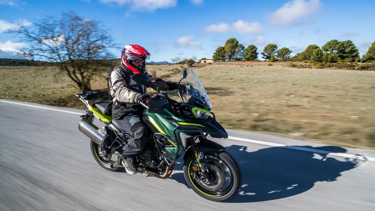 Motociclista en Benelli TRK 702 X, con opiniones positivas sobre su rendimiento en carretera abierta, rodeado de un paisaje rural.