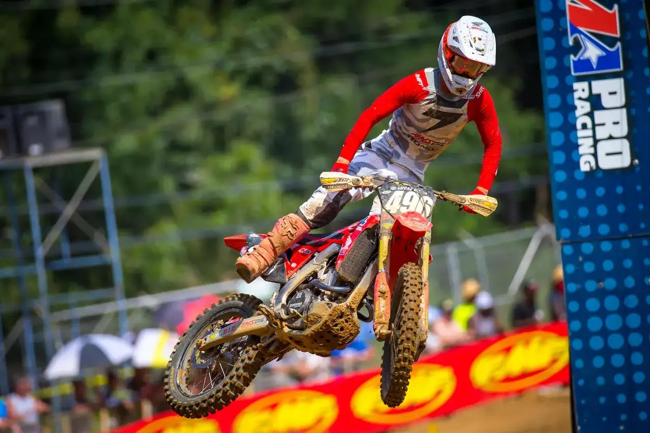 Jett Lawrence salta en su moto de motocross, con el número 49 en el manillar. El piloto luce un casco blanco y un traje rojo y gris.