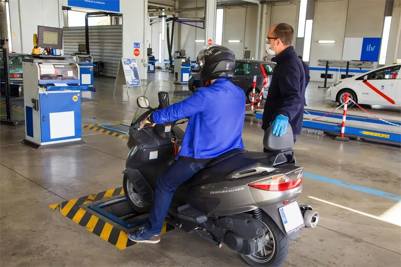 Un hombre en moto pasa la primera ITV. Un técnico con mascarilla supervisa la inspección en un centro de la ITV.