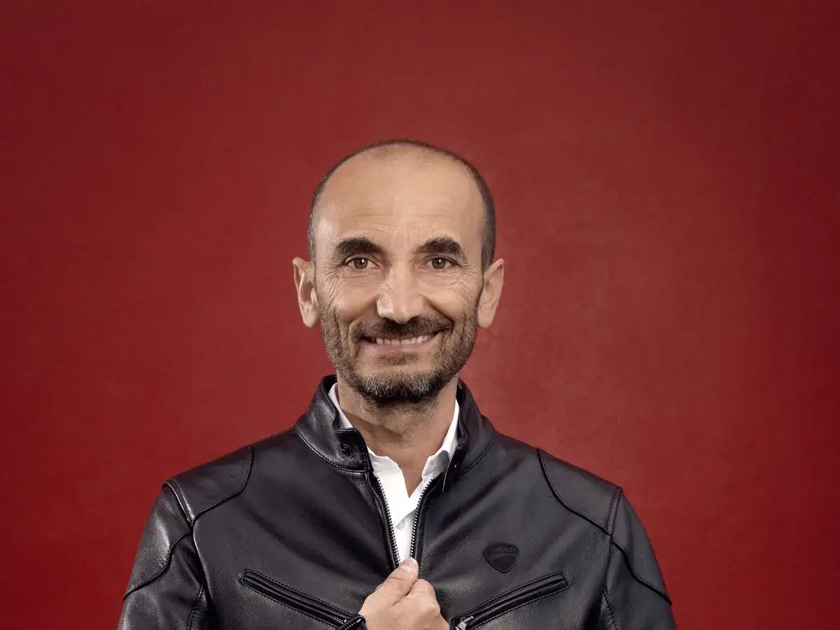 Claudio Domenicali, CEO de Ducati, sonríe con una chaqueta de cuero negra sobre fondo rojo.