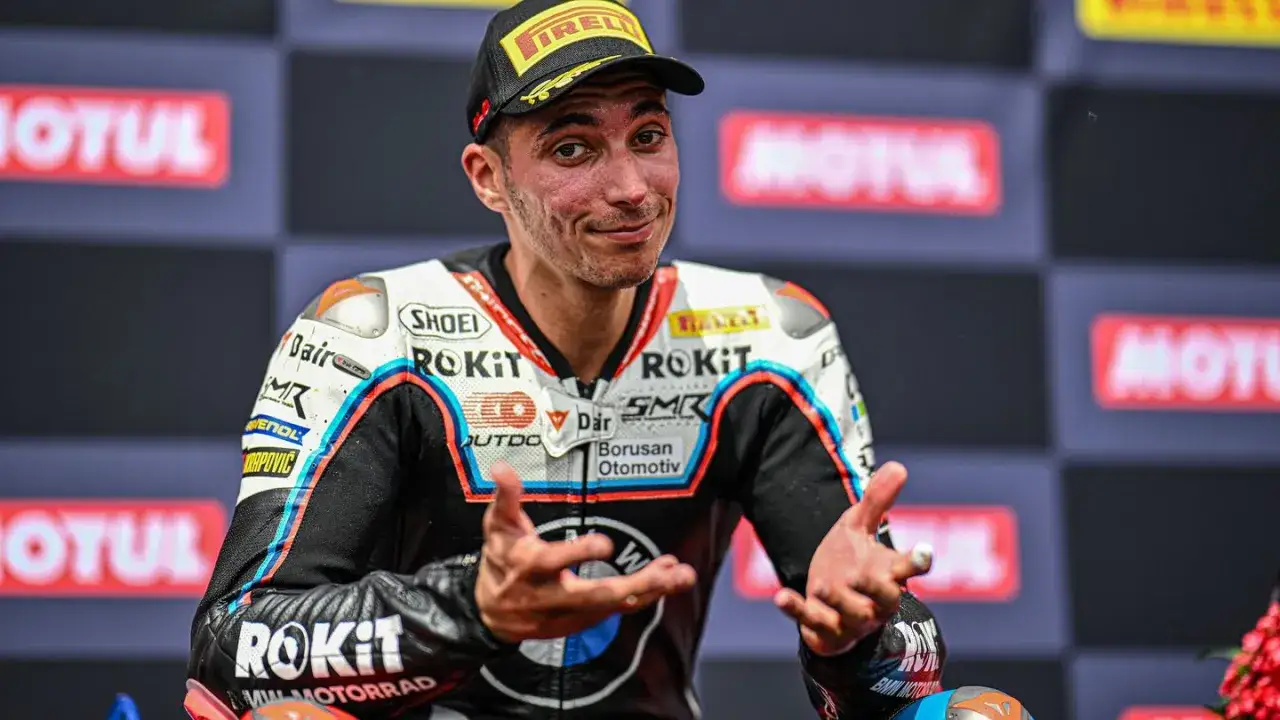 Toprak Razgatlıoğlu, piloto de Superbike, sonríe con gestos expresivos en el podio, luciendo su mono de competición.