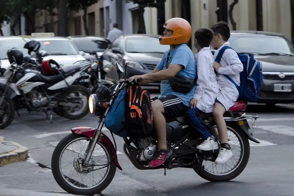 Un hombre lleva a dos ni&ntilde;os en moto, uno adelante y otro atr&aacute;s, todos con mochilas.