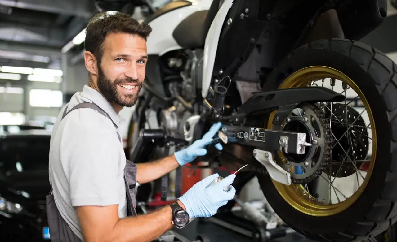 Mecánico sonriente revisa la cadena de una moto, preparándola para limitar moto a2.