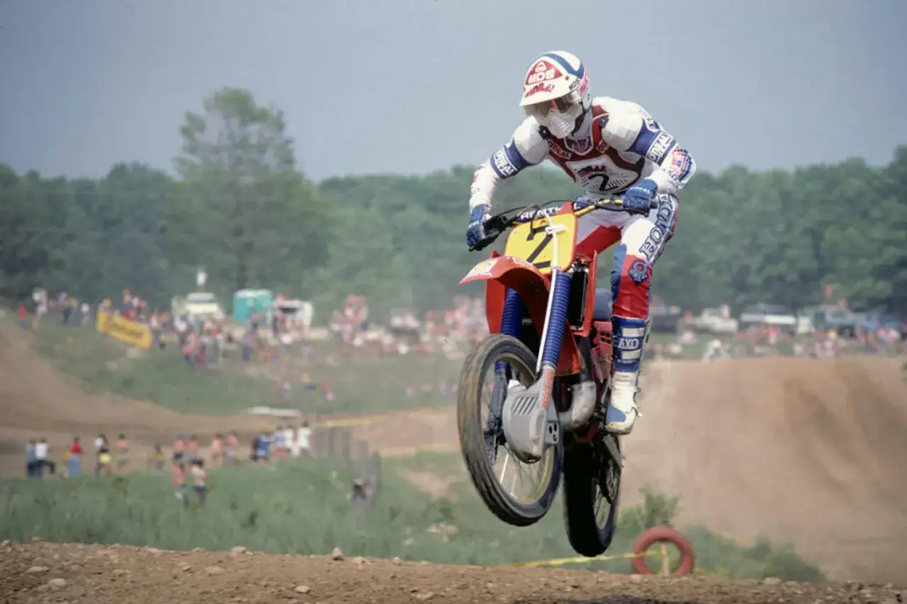 Motociclista Andre Malherbe salta en una carrera de motocross, con p&uacute;blico al fondo.