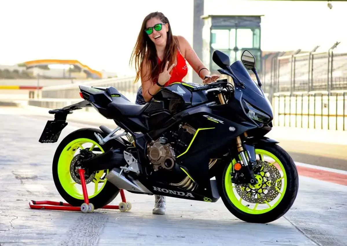 Chica sonriente con gafas verdes posa junto a una moto Honda CBR negra con detalles ne&oacute;n. &iexcl;Perfecta para motos r para el a2!