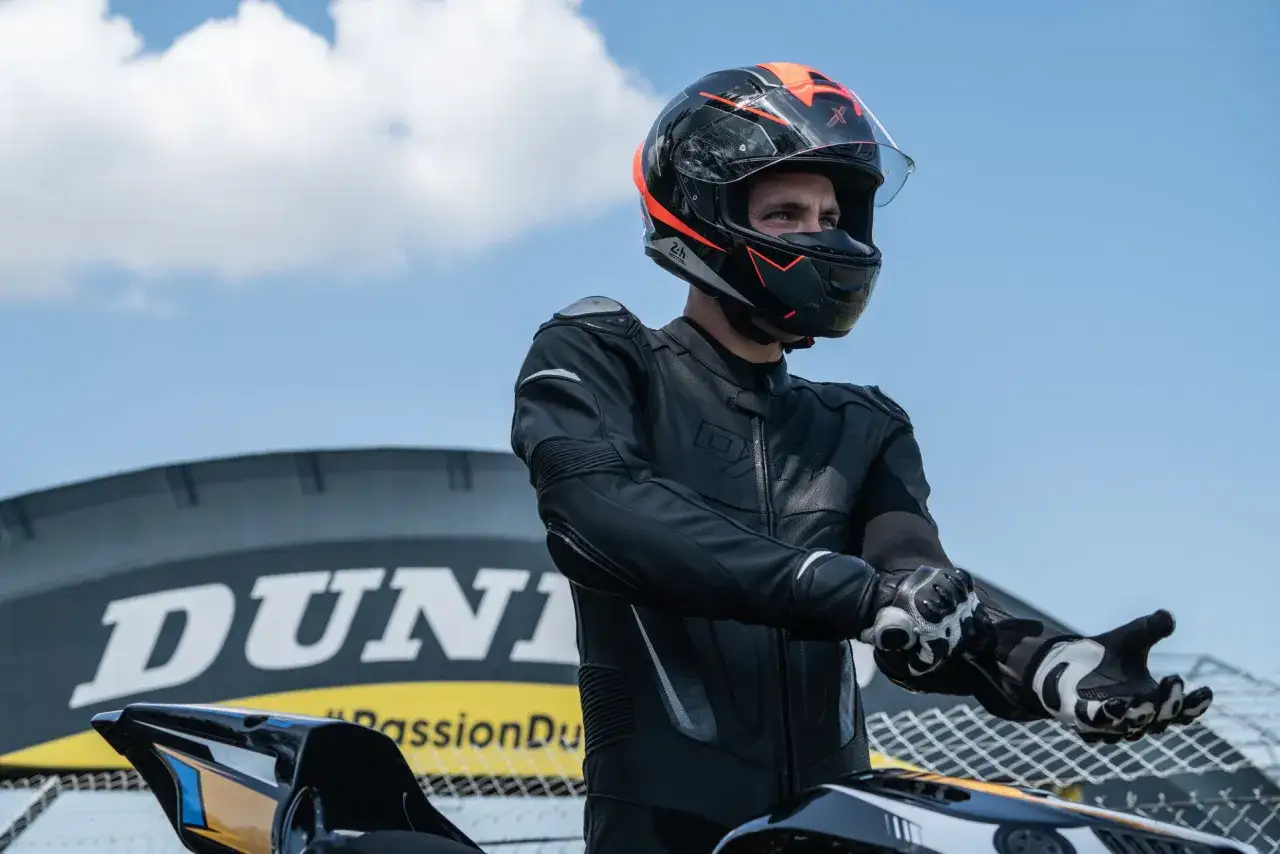 Piloto con casco y traje de cuero negro, listo para la carrera. Se aprecian los altos niveles de protecciones moto.