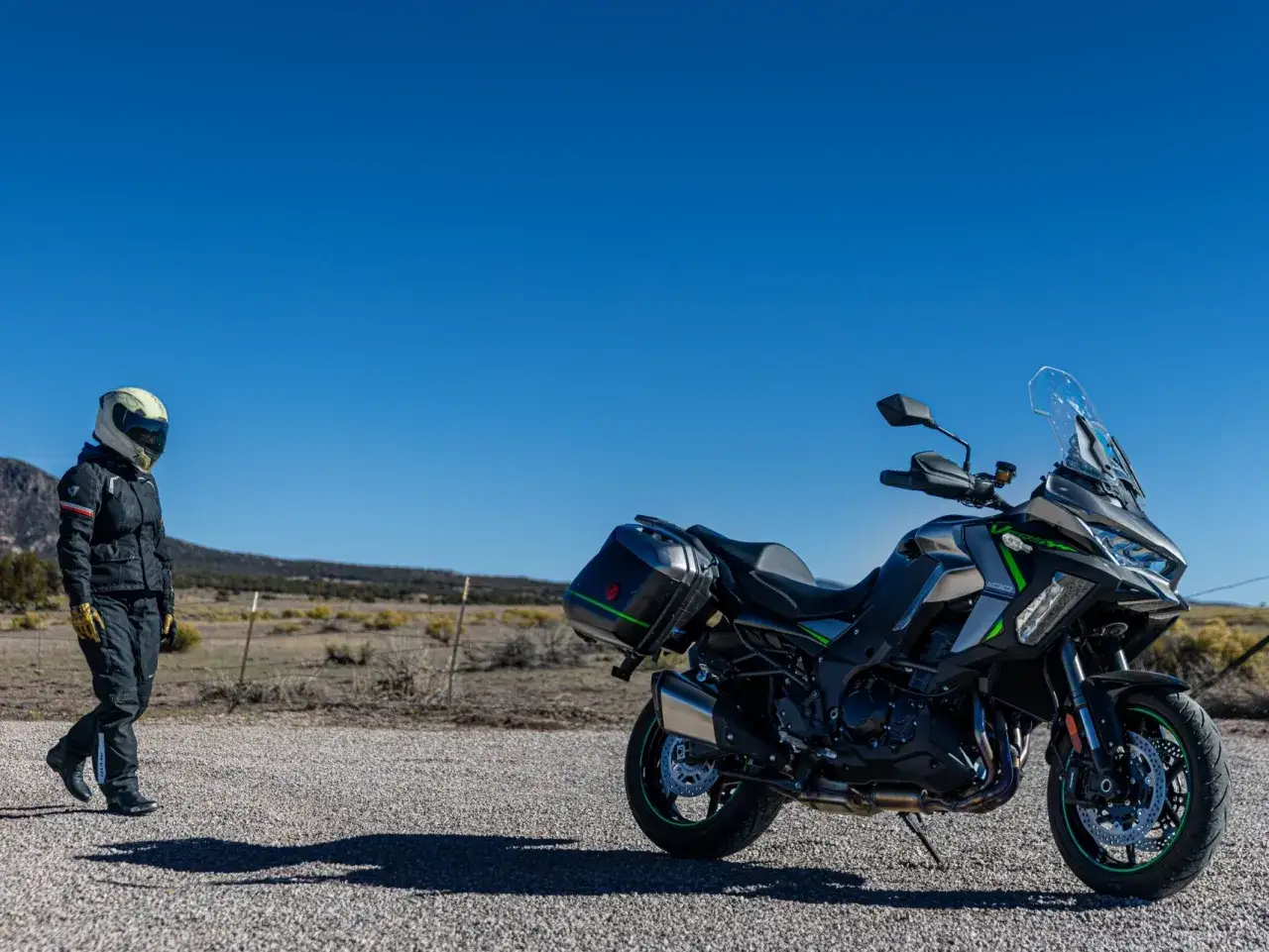 Motociclista se acerca a una moto sport turismo lista para la aventura en un paisaje desértico bajo un cielo azul.