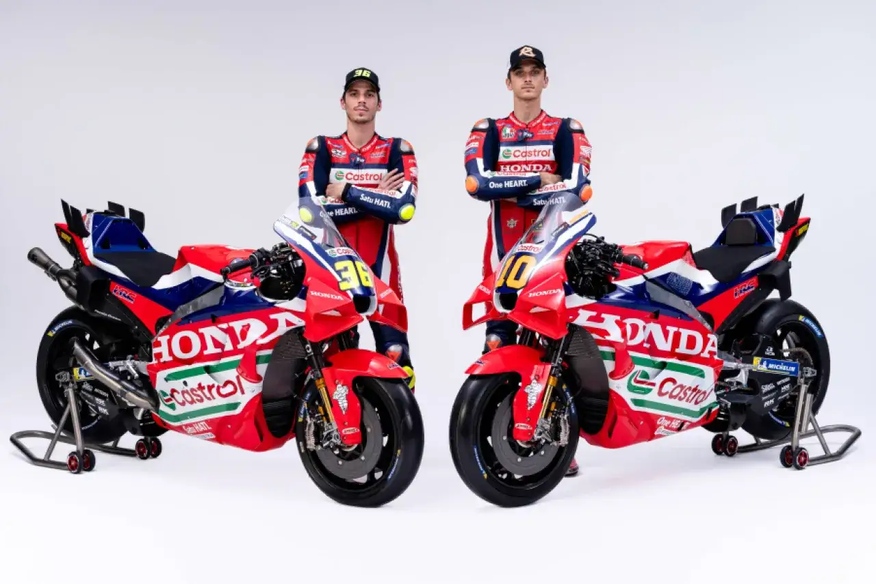 Dos pilotos de MotoGP posan junto a sus motos Honda HRC. Los colores rojo, blanco y azul dominan los trajes y las motocicletas, con el logo de Castrol.