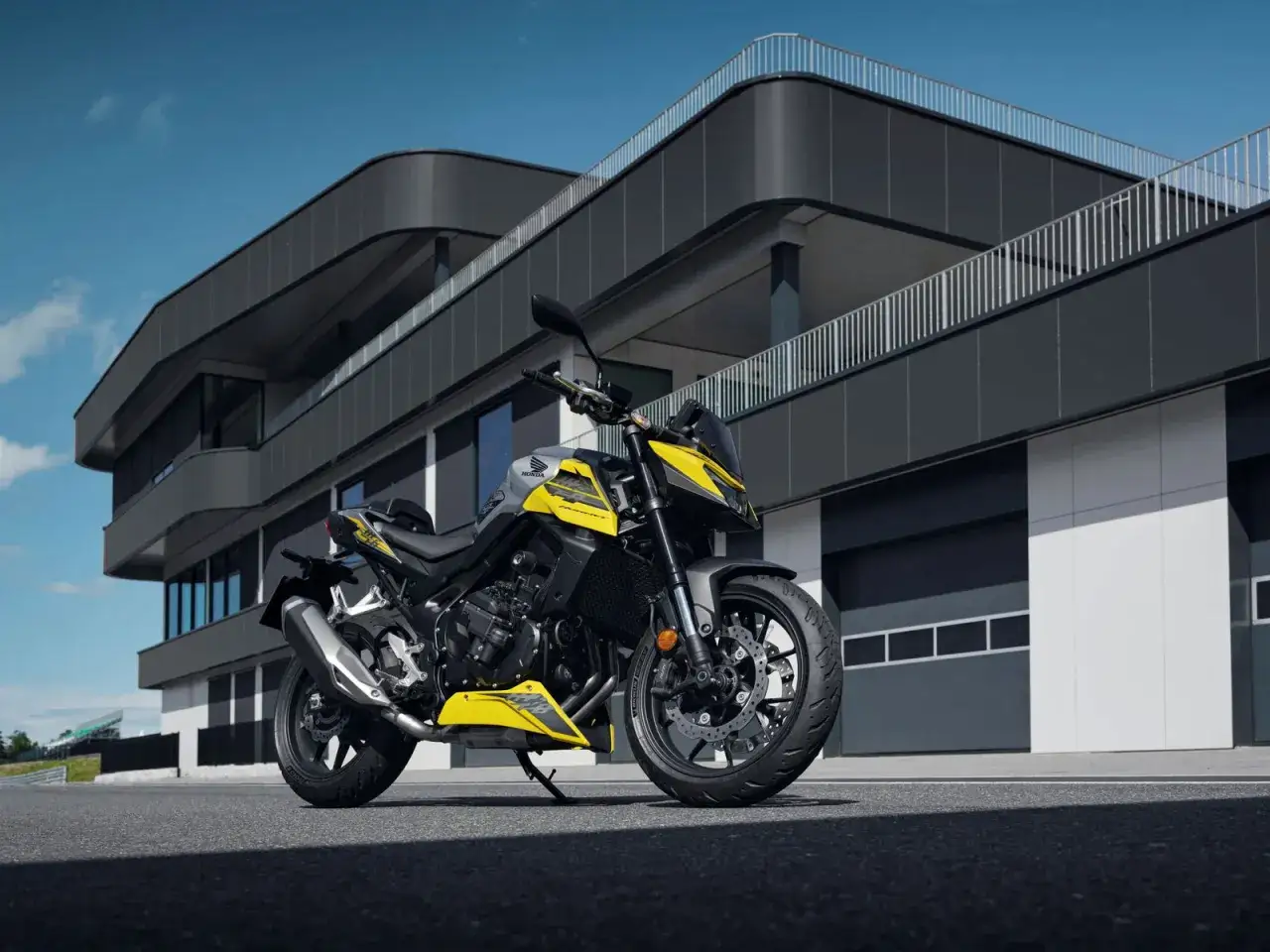 Honda Hornet 750 ficha técnica: una moto deportiva amarilla y gris aparcada frente a un edificio moderno.