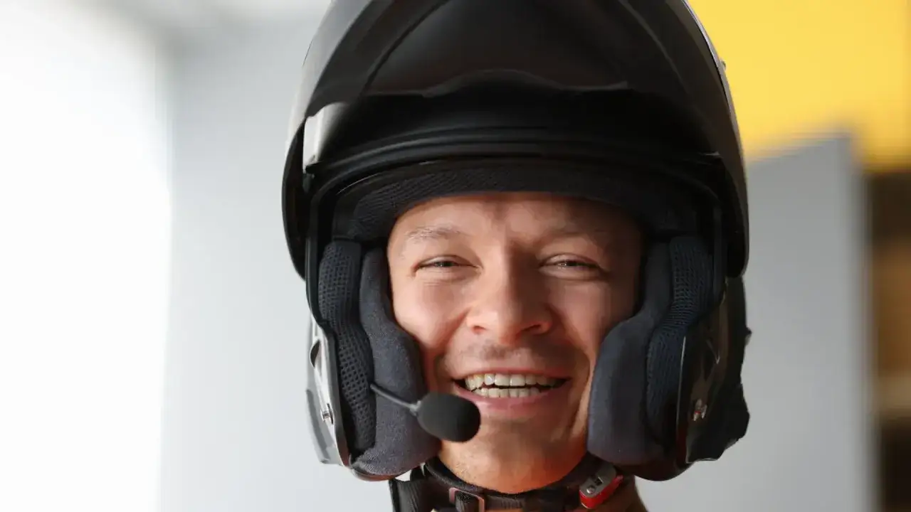Hombre sonriente con casco de moto y micrófono, listo para usar su intercomunicador moto legal y comunicarse en ruta.