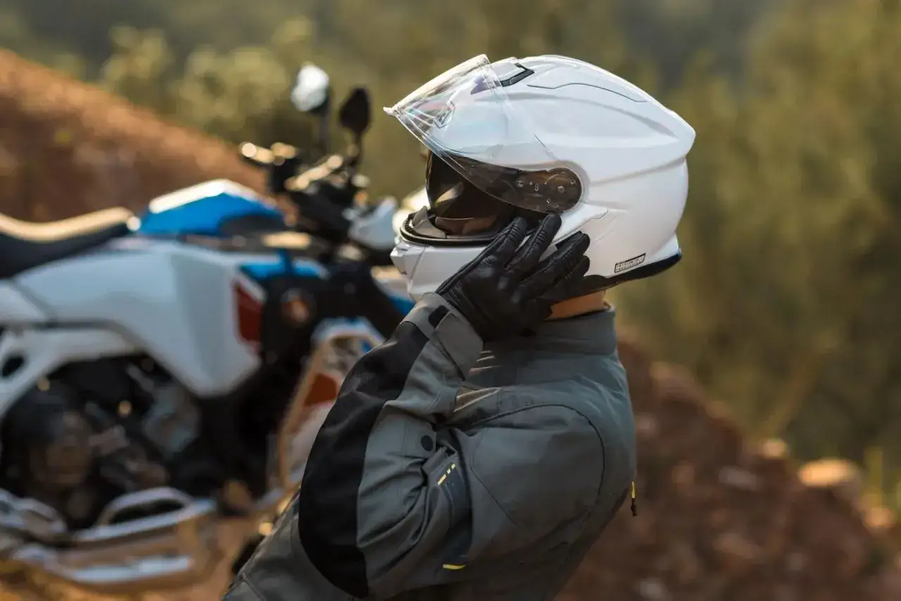 Motociclista ajustando su casco blanco Shoei NXR 2. Su peso es ideal para largas rutas.
