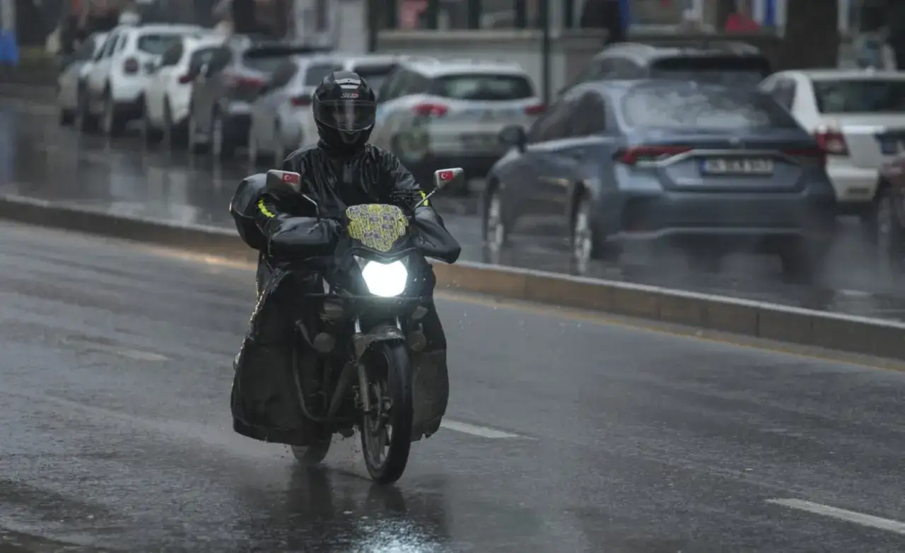 Motorista con casco y traje impermeable se prepara para conducir moto con lluvia en la ciudad, con autos en el fondo.