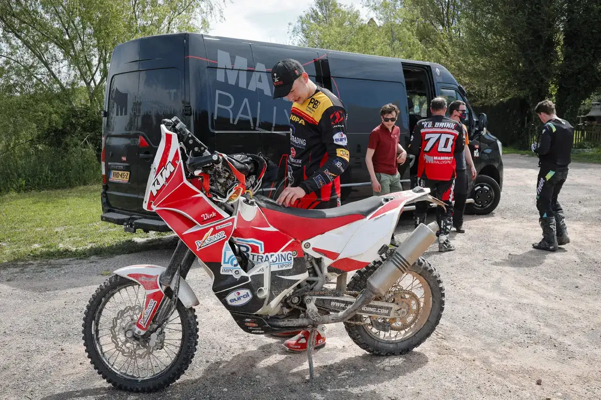 Jordi Viladoms, piloto de rally, revisa su moto KTM roja y blanca junto a un equipo y una furgoneta negra.