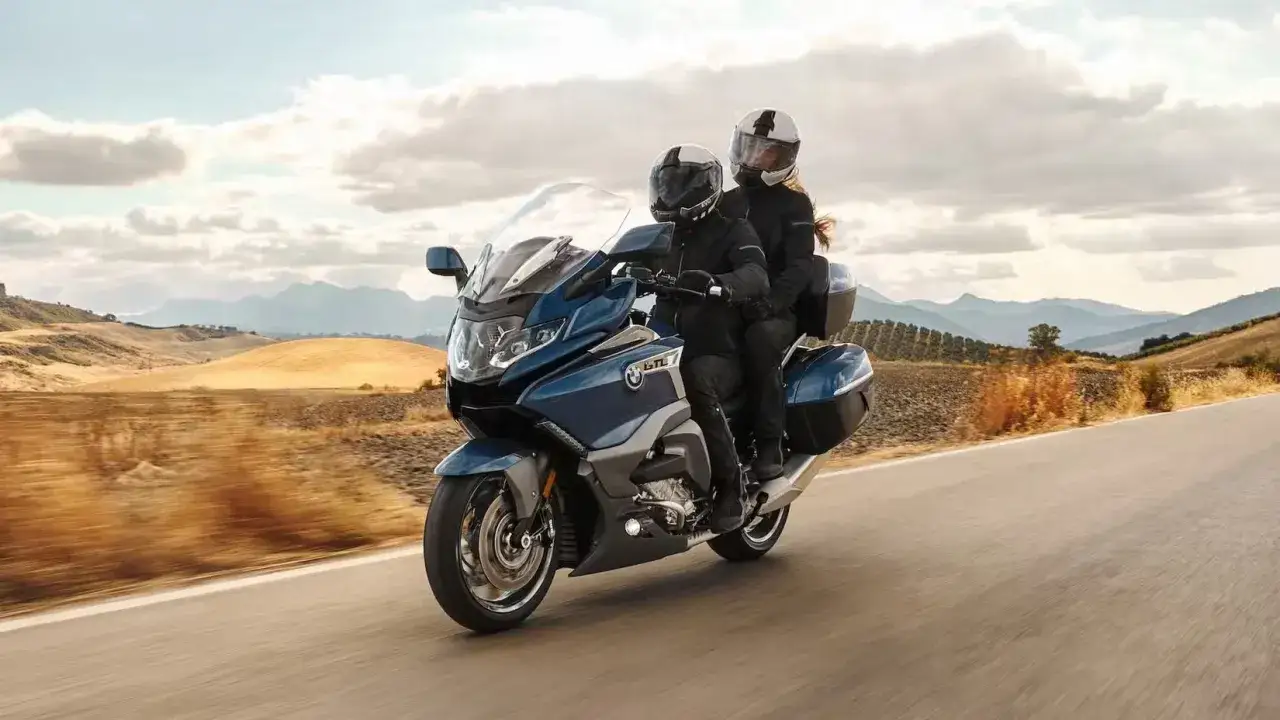Pareja disfrutando de un viaje en una moto azul, ideal para motos cómodas para viajar, con un paisaje montañoso de fondo.