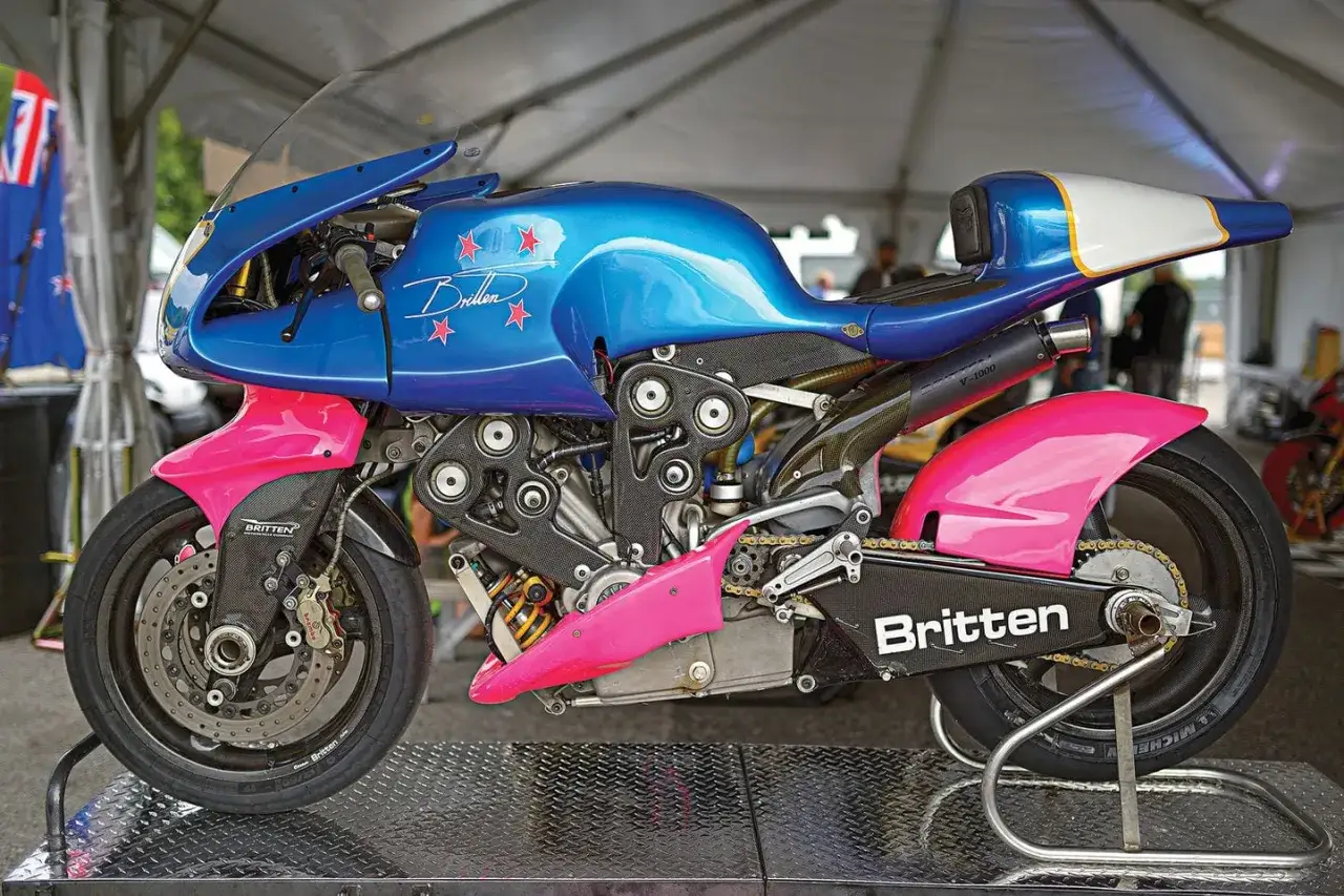 La Britten V1000, una moto de carreras azul y rosa con estrellas rojas, exhibe su motor V-twin y su diseño aerodinámico.
