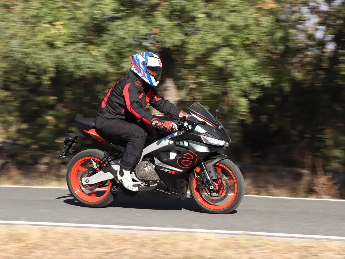 Motociclista en Aprilia RS 457, con detalles de su ficha técnica en mente, recorre una carretera rodeada de árboles.